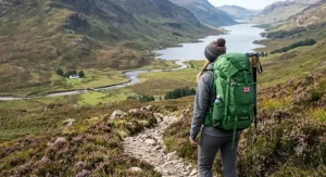 A hiker pausing to look at the view over a Lake District mere, wearing a green women's backpacking rucksack