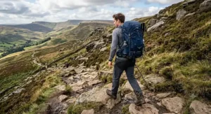 A male walker wearing a navy blue 40l hiking rucksack navigating a rocky path in the Peak District