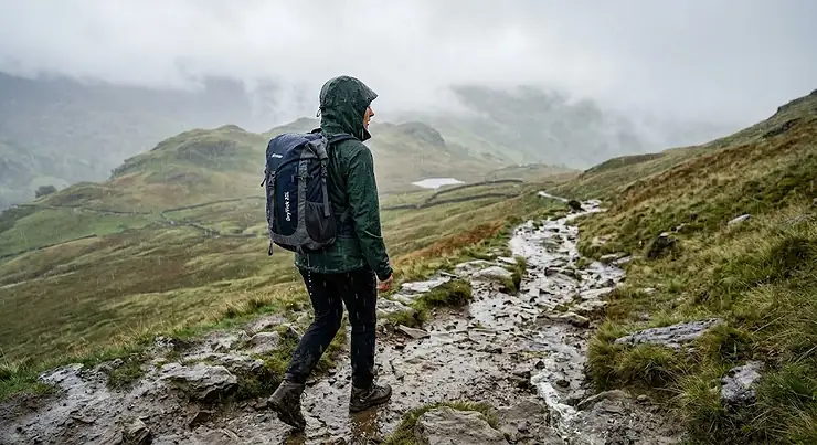 Hiker wearing the best waterproof daypack during a rainy trek through the Lake District hills.