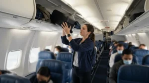 Placing a soft-sided wheeled holdall for cabin baggage into an aeroplane overhead locker.