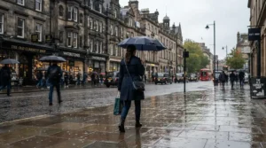 A commuter wearing a waterproof laptop backpack while walking past a red telephone box in a London drizzle.